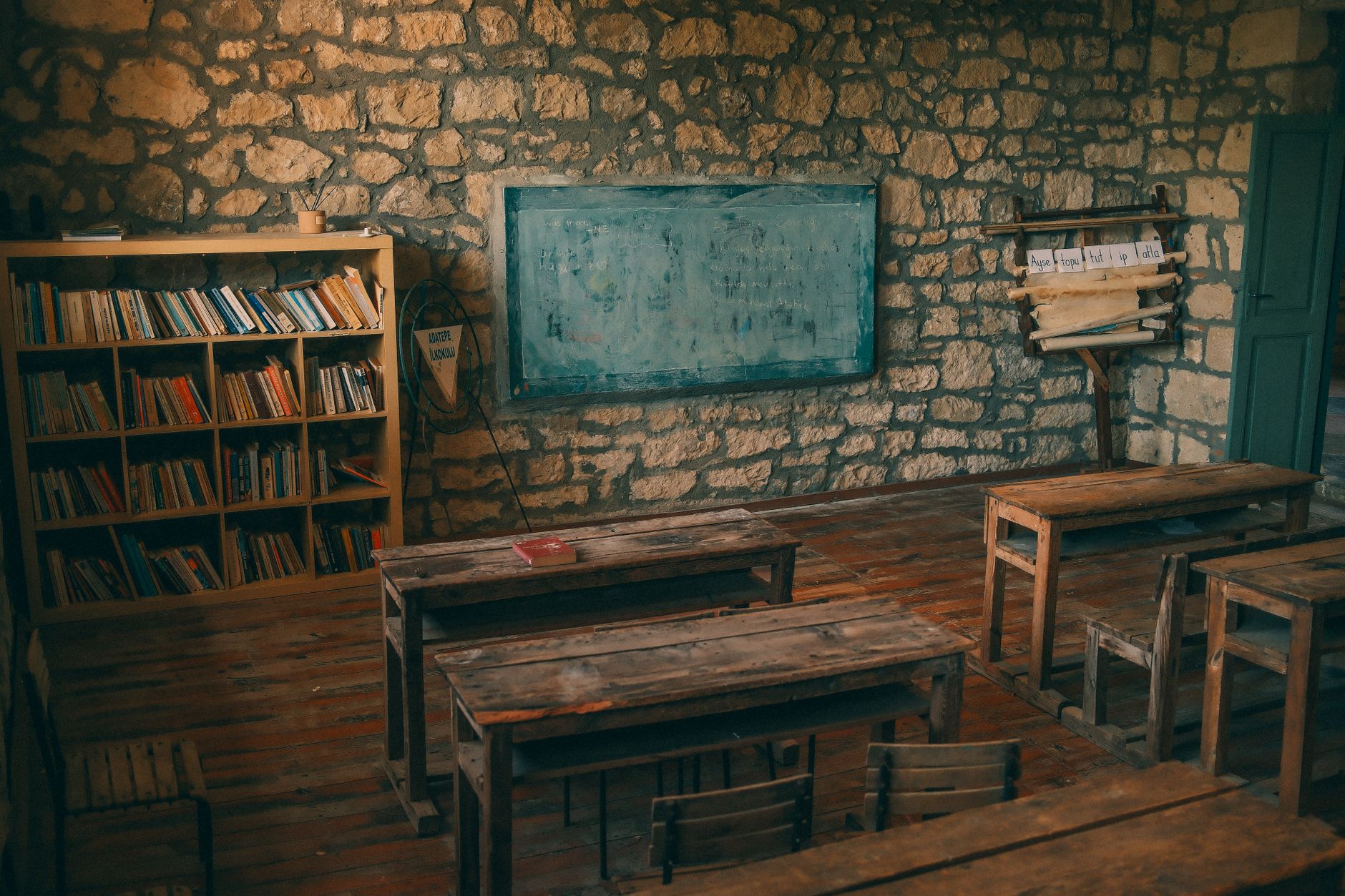 Aula vac&iacute;a con bancos de madera, biblioteca y pizarr&oacute;n en una construcci&oacute;n de piedra