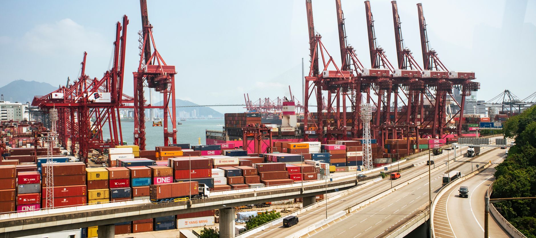 Grúas portuarias rojas, contenedores y camiones en una terminal de carga