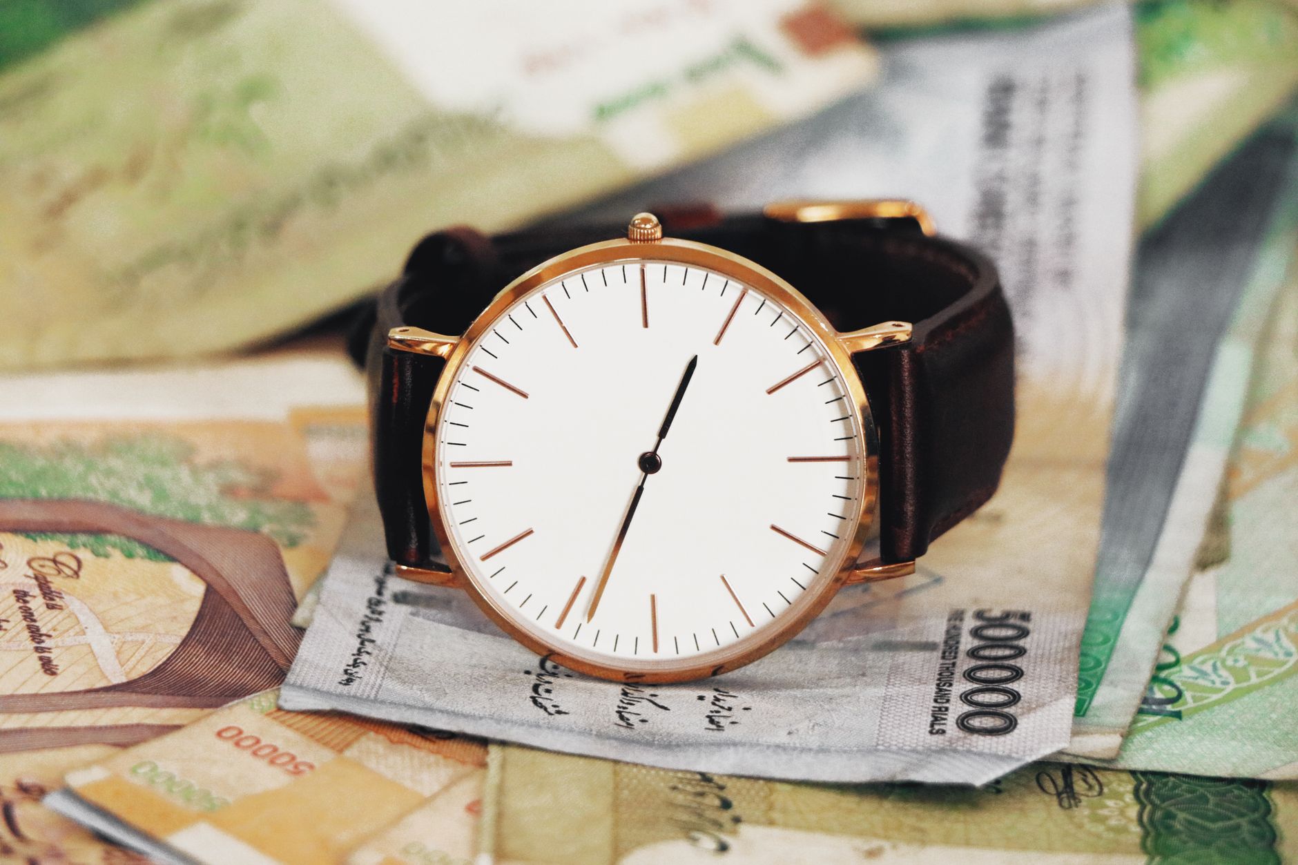 Billetes de rial iraní junto a un reloj, imagen ilustrativa de la depreciación de la moneda